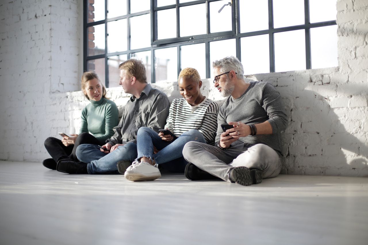 A diverse group of adults relaxing indoors, chatting and using smartphones.